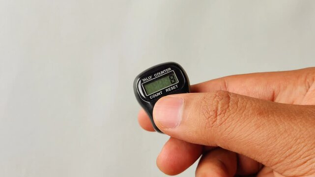A close-up footage of a hand using digital prayer beads, commonly used by Muslims for dhikr (remembrance of God). The digital counter helps in tracking recitations or meditation counts.