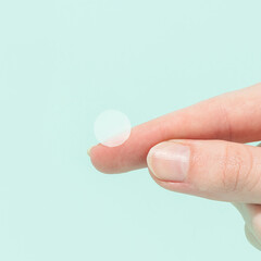 Woman holding hydrocolloid pimple patches on finger with mint blue background