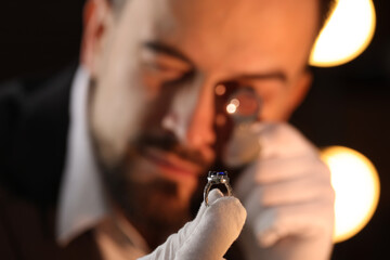 Appraiser with loupe evaluating luxury ring indoors, selective focus