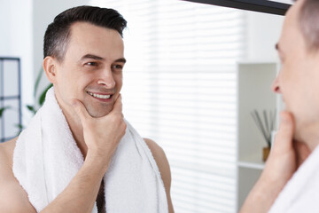 Smiling man after shaving looking at mirror in bathroom