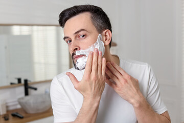 Handsome man applying shaving foam in bathroom