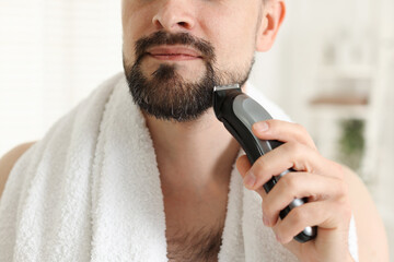 Man shaving with trimmer at home, closeup