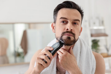 Handsome man shaving with trimmer in bathroom