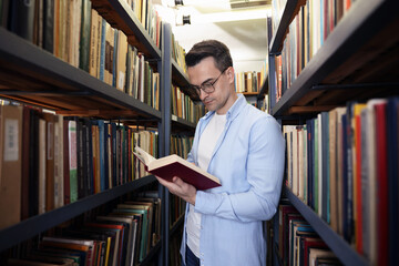 Man reading book near shelves in public library