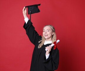 Happy student with diploma and mortarboard after graduation on red background