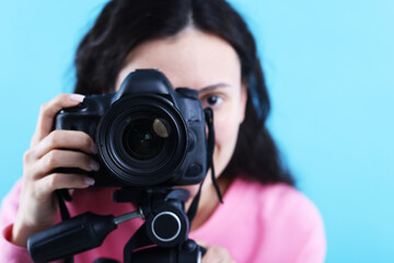 Woman with professional video camera on light blue background, selective focus