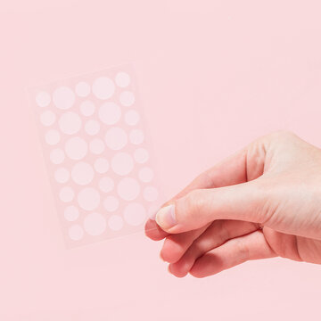 Woman holding set of hydrocolloid pimple patches on pink background