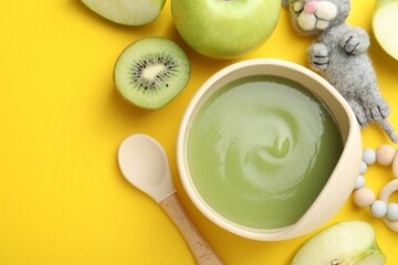 Baby food. Tasty puree in bowls, different ingredients and toys on yellow background, flat lay....