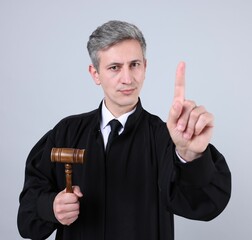Judge with mallet shaking finger on grey background