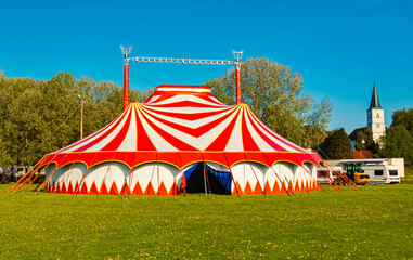 Spring landscape with a red and white circus tent and a church on a sunny day at Postmuenster, Rottal Inn, Bavaria, Germany
