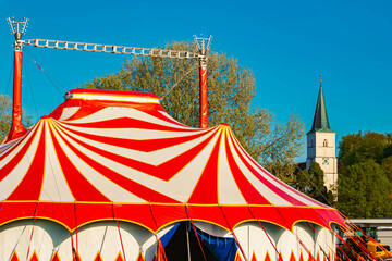 Spring landscape with a red and white circus tent and a church on a sunny day at Postmuenster, Rottal Inn, Bavaria, Germany