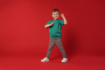 Happy little boy dancing on red background, space for text