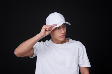 Young man wearing stylish white baseball hat on black background