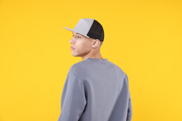 Young man wearing stylish baseball hat on yellow background