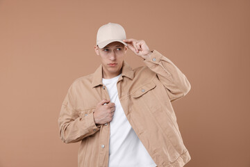 Young man wearing stylish beige baseball hat on light brown background