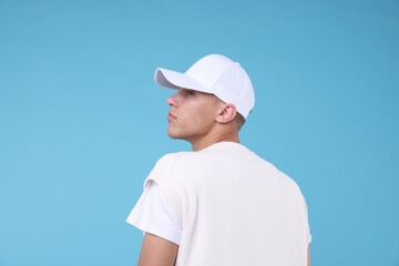 Young man wearing stylish white baseball hat on light blue background