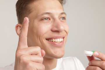 Man with contact lens and case on light background, closeup