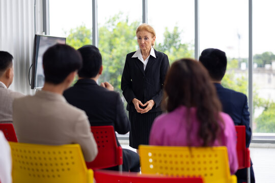 Public speaking training in seminar : senior caucasian ceo business female leader in seminar, speaking on business training with group of diverse people company employees in meeting room