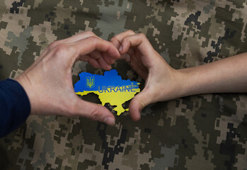 Female and child hand folded in shape of heart around yellow and blue map of Ukraine on background...