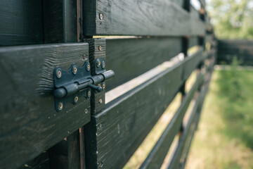 Close-up view of a black wooden fence with a metal latch, captured at an angle in daylight
