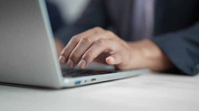 Professional businessman working intensely on laptop, hands typing rapidly while browsing internet and searching critical business information in modern corporate workplace