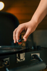 Close-up of hand placing needle on vinyl record on turntable, cozy warm lighting and shallow depth of field enhance vintage atmosphere