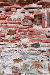 Rugged surface of historical brickwork combining reddish bricks with natural stone plates embedded in cement, showcasing traditional construction.Closeup textured brick wall with ancient layered stone
