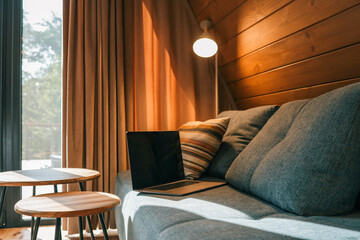 Laptop on a blue couch in a cozy wooden living room with warm natural light, striped pillow, round...