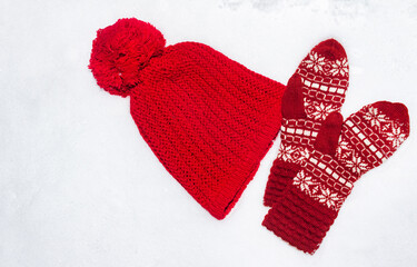 Photo of knitted hat and gloves laying on snow.