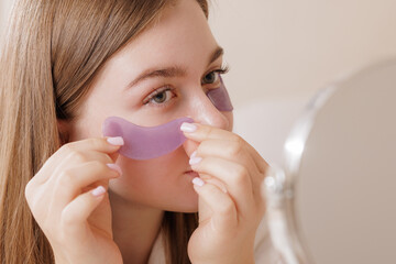 Woman uses purple under-eye patches for hydration, de-puffing, and skin rejuvenation, highlighting a modern beauty and skincare routine.