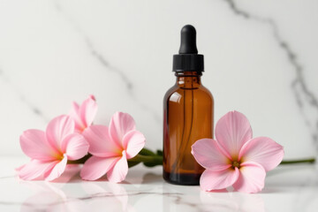 A bottle of essential oil sits on a marble surface surrounded by pink flowers