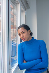 Vertical portrait Young latin hispanic woman with sad face next to a window on cold day of winter...