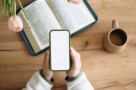 Phone in hand with isolated screen, on the home background with Bible.