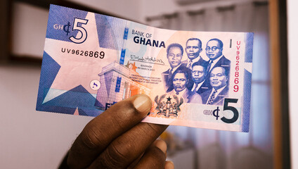 closeup of Black person hands inspecting and checking pointing raising 5 Ghanaian cedi note. watermark on money. Verification of paper currency not fake counterfeit original real