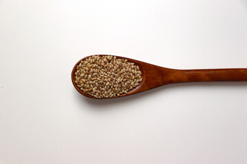 Roasted sesame seeds on a wooden spoon. White background.