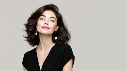 Fototapeta premium Woman with long hair and earrings is smiling. She is wearing a black dress and is standing in front of a white background
