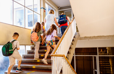 Teacher with schoolkids walking on stairs on school hallway.
