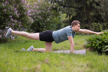 Young man practicing yoga on mat in park