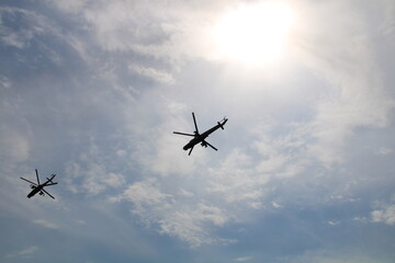 2 helicopters flying in the sky against the background of the sun