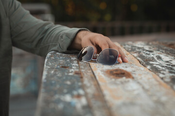 Male Hand in Linen Shirt Holding Sunglasses on Wooden Table