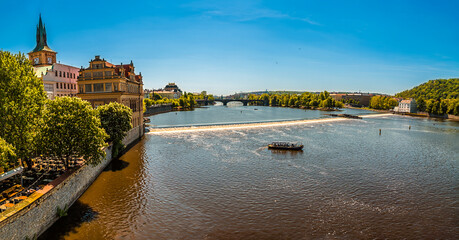 Obraz premium A view from the Charles Bridge up the Vltava river towards the weir across the river in Prague in springtime
