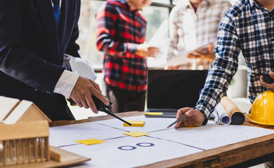 Architect discussing housing project with blueprints and miniature house. Architects gather in...