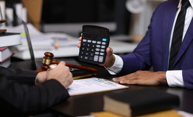 Lawyers discussing legal fees using calculator in law office. Two lawyers are discussing legal fees for a new contract using a calculator, highlighting the financial aspects of legal representation.