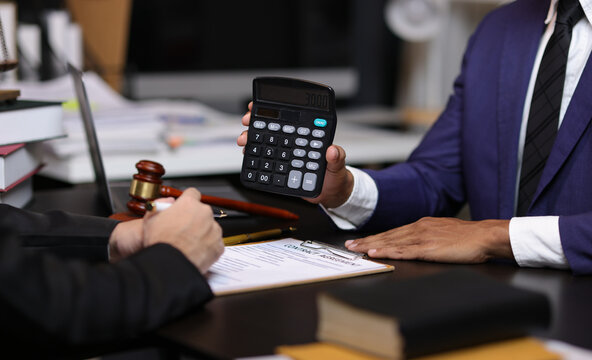 Lawyers discussing legal fees using calculator in law office. Two lawyers are discussing legal fees for a new contract using a calculator, highlighting the financial aspects of legal representation.
