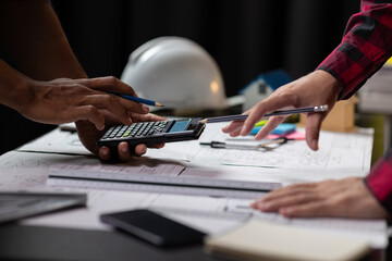Architect using calculator calculating construction costs on blueprint. Architects collaborating at...