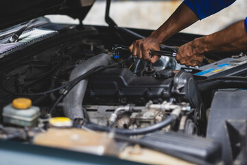 Auto mechanic repairing engine using wrench in garage. Mechanic in a jumpsuit fixes a car engine in a garage workshop.