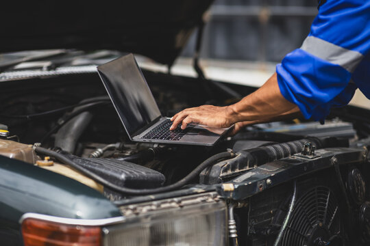 Car mechanic running diagnostics on vehicle using laptop.