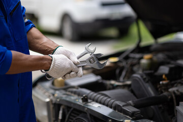 Auto mechanic repairing engine using wrench in garage. Mechanic in a jumpsuit fixes a car engine in...