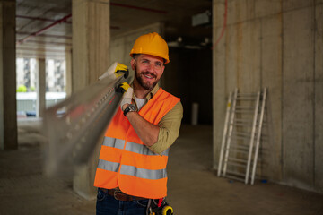 Smiling construction worker wearing a safety vest and helmet, carrying a long metal beam on his...