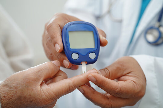Asian doctor using digital glucose meter for check sample blood sugar level to treatment diabetes.